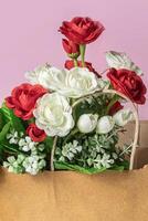 Bouquet of red and white roses in paper bag on pink background, close-up photo