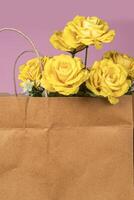 Bouquet of artificial yellow roses in paper bag on pink background. Place for text. photo