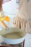 Woman Pouring Cooking Oil from Bottle into Frying Pan on Stove photo