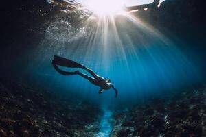 Young freediver woman with fins glides and amazing sun rays. Freediving underwater in ocean photo