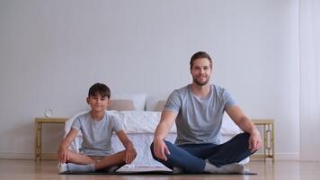 Family fitness at home, Father coach, Sports kid, Fun gymnastics. Man and boy doing yoga at home while sitting on the floor and looking at the camera video