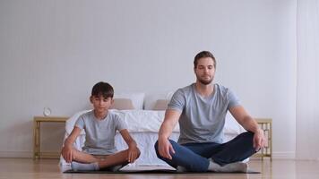 familie geschiktheid Bij huis, vader coach, sport- kind, pret gymnastiek. Mens en jongen aan het doen yoga Bij huis terwijl zittend Aan de verdieping video