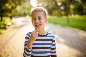 retrato de contento chico quien es en pie en parque y comiendo hielo crema. foto