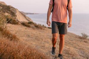 Bottom part of man with backpack walking on sea coastline with warm sun light. photo