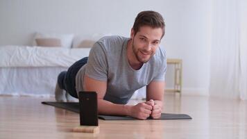 Family fitness at home, Father coach, Sports kid, Fun gymnastics. Attractive man doing sports exercise lying on the floor at home and timing the time on his smartphone. Looking into the camera video