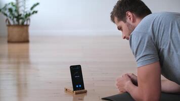 Family fitness at home, Father coach, Sports kid, Fun gymnastics. Young man doing sports exercise while lying on the floor at home using stopwatch in smartphone video