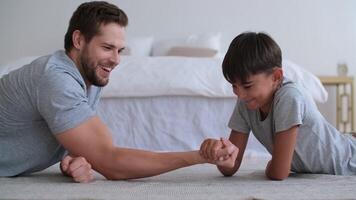 família ginástica às lar, pai treinador, Esportes criança, Diversão ginástica. Papai e filho estão brigando com seus mãos deitado em a chão do a casa video