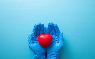 Hand in medical glove hold red heart sign. photo