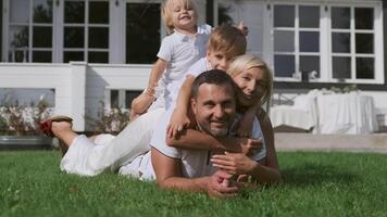 contento familia con niños teniendo divertido acostado en cada otro cerca el casa en el césped. familia felicidad. cámara moverse Derecha video