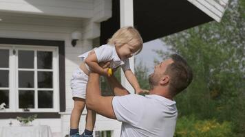 joven brutal padre y pequeño chico tener divertido cerca el casa en el calle. un hombre sostiene un niño en su brazos y levanta arriba video