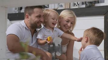 contento giovane famiglia di quattro con bambini avendo divertimento e giocando con ogni altro mentre giocando su il veranda nel il Casa. mamma papà e Due figli maschi video