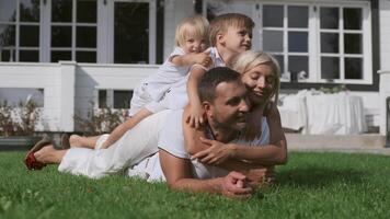 Happy family with children having fun lying on each other near the house on the grass. Family happiness video