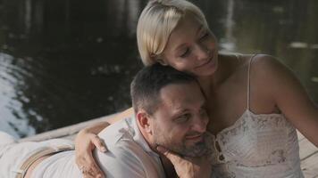 A young loving couple in white clothes is resting on the pier on a sunny day. Portrait video