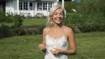 Beautiful young girl with blond hair in white clothes is walking on the grass and smiling. video