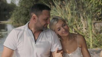 Jeune aimant couple sont séance sur le jetée sur une ensoleillé journée et souriant. lent mouvement video