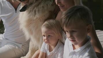 ung skön familj med barn och med en hund ha en resten Sammanträde på en pir nära de sjö. långsam rörelse. närbild video