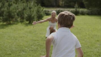 une peu garçon dans blanc vêtements se réjouit et court à le sien bien-aimée mère. maman câlins sa fils. tournage de derrière video