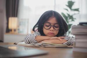 Little Asian girl sitting alone and looking out with a bored face, Preschool child laying head down on the table with sad bored with homework, spoiled child photo
