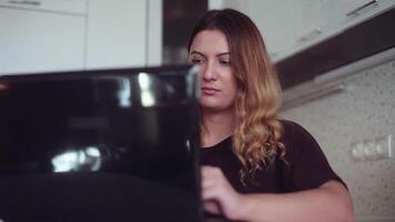 Close-up. Beautiful young business woman with long hair chatting on mobile computer in black color at home sitting at table with good mood and smiling. video