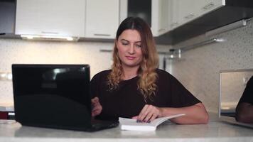 Beautiful young business woman with a long dark hair working behind a mobile computer with a diary at home sitting at a table. HD video