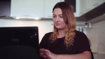 Beautiful young business woman with a long hair prints on a mobile computer at home sitting at a table with a good mood. video