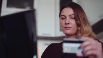 de cerca. un hermosa joven mujer con largo pelo entra el crédito tarjeta datos dentro el en línea Tienda utilizando un móvil computadora. hogar estilo. video