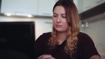 Beautiful young female with long dark hair in dark clothes working at computer at home sitting at table video