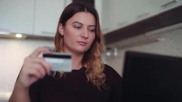 avvicinamento. bellissimo donna con lungo buio capelli in linea bancario con un' computer topo su il Internet con un' credito carta a casa a un' tavolo con un' bene umore video