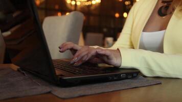 Close-up. Beautiful business woman with blond hair in business clothes typing text on a mobile computer sitting at a table in a cafe. video