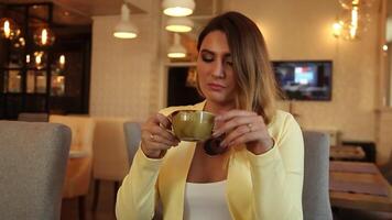 lindo o negócio mulher dentro o negócio roupas bebendo chá dentro uma cafeteria sentado às uma mesa tendo uma Boa humor. HD. o negócio estilo video