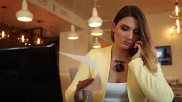 Close-up. Beautiful business woman with long blond hair in business clothes working with documents sitting at the table and discussing issues with a colleague on the phone in a cafe. HD. video