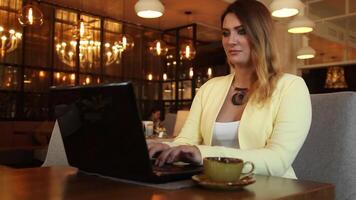 hermosa negocio mujer con largo pelo corriendo utilizando un móvil computadora de oscuro color en un café en el noche para un taza de té video
