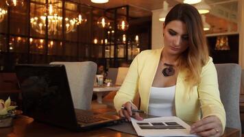 lindo o negócio mulher com grandes loiro cabelo dentro o negócio roupas trabalhando com documentos sentado às uma mesa dentro uma cafeteria video