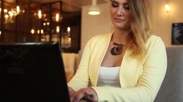 Close-up. Beautiful business woman with blond hair in business clothes typing text on a mobile computer sitting at a table in a cafe having a good mood. HD. video