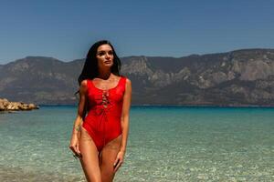 Beautiful young woman in a red swimsuit standing at sea beach photo