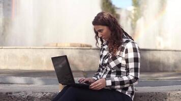 beautiful young business woman using laptop at break outdoors drinking coffee. beautiful female student sitting on a fountain video