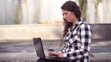 avvicinamento. giovane bellissimo contento attività commerciale donna con lungo capelli stampe su mobile computer seduta su il le scale nel il città video