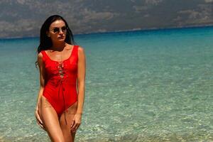 Beautiful young woman in a red swimsuit standing at sea beach photo