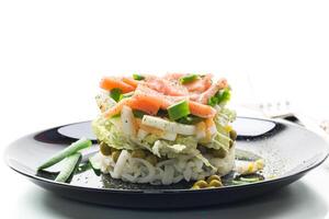 Layered salad of cabbage and other vegetables with pieces of red fish in a plate. photo