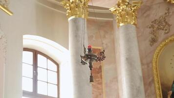 minsk, bielorrusia, 2014 - hermosa antiguo falsificado colgando lámpara con monogramas en interior de Iglesia cerca ventana y icono con Virgen María. templo con columnas con capital decorado con oro hoja. video