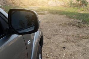 Car on the road in the countryside, view from the side mirror with fron car. Background of soil and green grass on the ground. photo