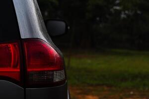 Beside of car and tail lights of the car were wet with water droplets. Background of green grass and trees in the dark tone at evening. photo