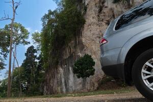 Beside of grey car can see with glass and wheels. Parking in the park. Background of dirt roads and high mountains and forests. photo