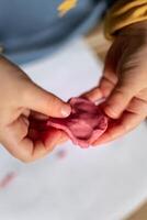 niño teniendo divertido modelado sal masa, auténtico actividad con natural rosado colorante remolacha jugo, multa motor habilidades desarrollo foto