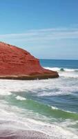 maravilloso rojo arena playa con un hermosa ver de el Oceano y rocoso colinas video