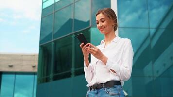 sonriente mujer de negocios utilizando teléfono inteligente y ondulación fuera de oficina video