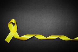 childhood cancer awareness day. Yellow ribbon on black background. photo