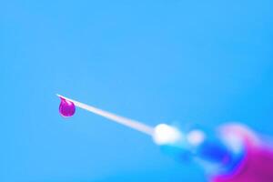 Macro of hypodermic needle. drop of pink drug photo