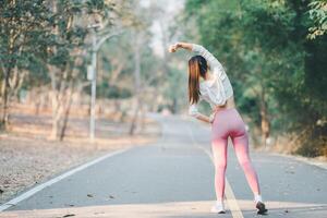 Fitness and running concept, Back view of a woman stretching arms upwards, preparing for a run on a tranquil park road surrounded by trees. photo