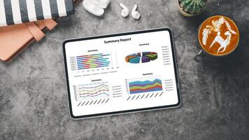 Business analytics concept, A digital tablet on a marble surface showing graphs and pie charts in a business summary report, alongside a coffee and earbuds. photo